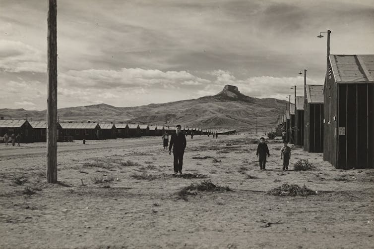 A black and white image of a desolate landscape with rows of buildings stretching into the distance and a mountain on the horizon.