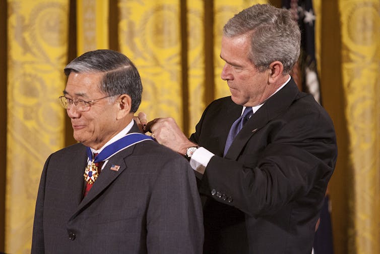 One man fastens an award ribbon around the neck of another man.