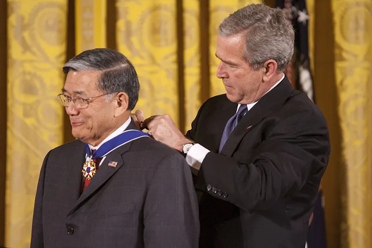 One man fastens an award ribbon around the neck of another man.