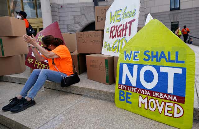 A woman sitting on steps in Boston claps next to piles of boxes and protest signs against conviction
