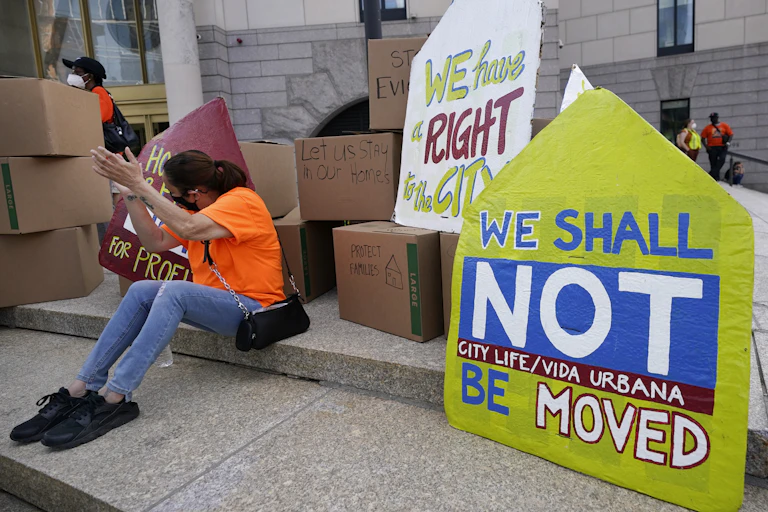 A woman sitting on steps in Boston claps next to piles of boxes and protest signs against conviction