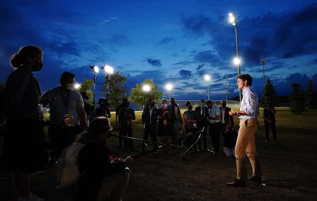 Trudeau speaks to the media at dusk, with floodlights around and above him.
