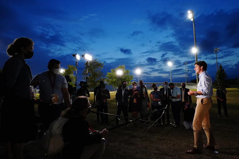 Trudeau speaks to the media at dusk, with floodlights around and above him.