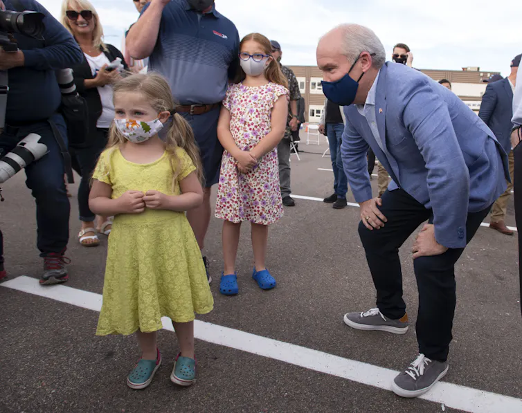 Erin O'Toole leans on his knees to speak to a young girl.