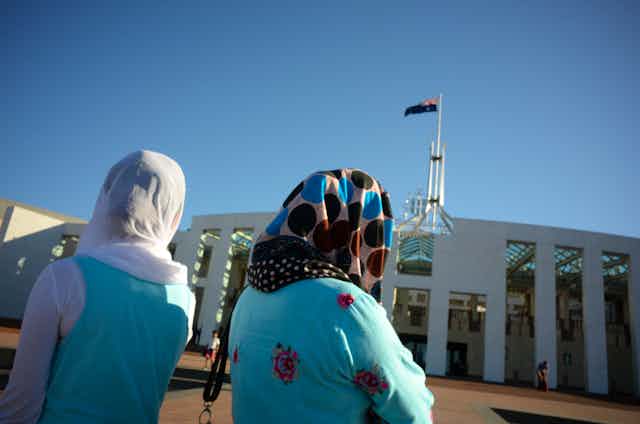 Two women wearing headscarves look at Parliament House in Canberra.