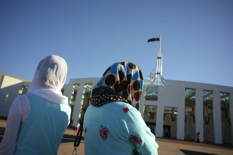 Two women wearing headscarves look at Parliament House in Canberra.