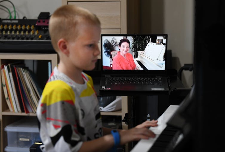 boy at piano gets a music lesson via online video link from his teacher