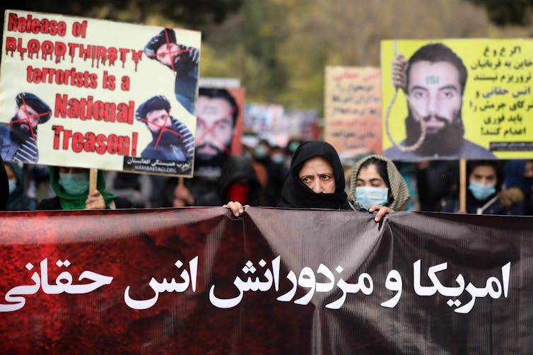 Afghan women stand with banners protesting the release of senior terrorist leaders including Anas Haqqani.