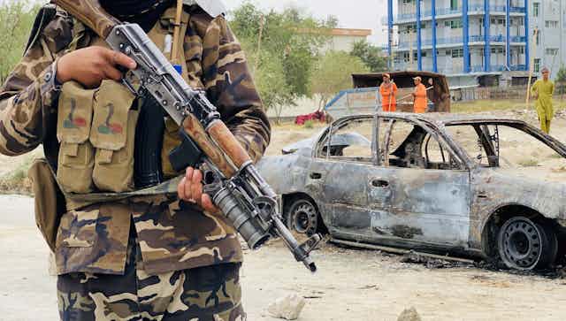 A Taliban fighter with an automatic rifle stands guard over a car used to fire rockets at Kabul airport, August 2021.