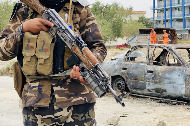 A Taliban fighter with an automatic rifle stands guard over a car used to fire rockets at Kabul airport, August 2021.