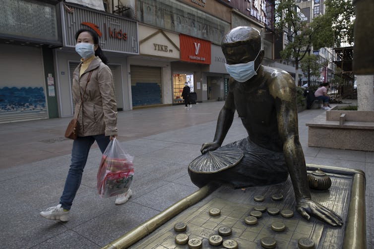 A woman wearing a surgical mask walks past a statue wearing a surgical mask.