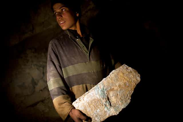 A young Afghan miner carries a large stone.