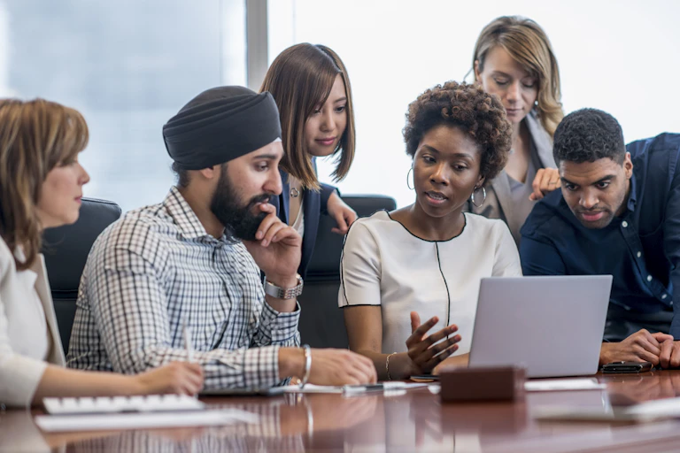 A diverse group of adults gather around a laptop.