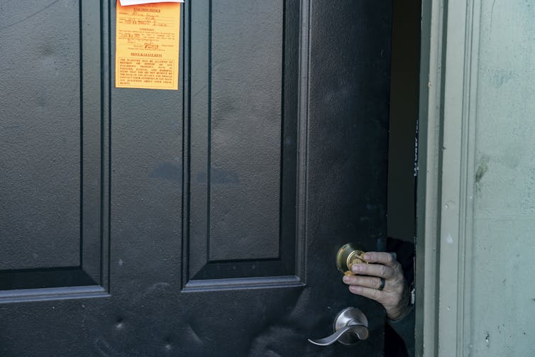 A worker's hand is visible on a door lock below an orange notice of eviction.