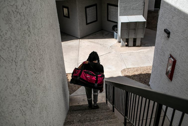 A person carrying a large duffel bag descends a staircase