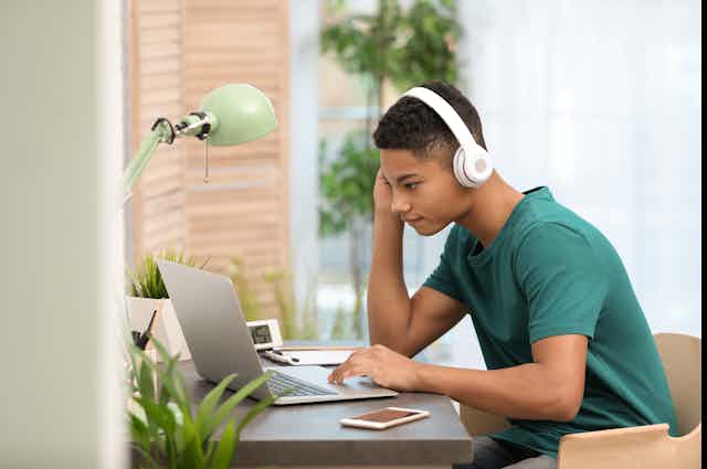 Jeune homme avec des écouteurs, penché sur son ordinateur portable