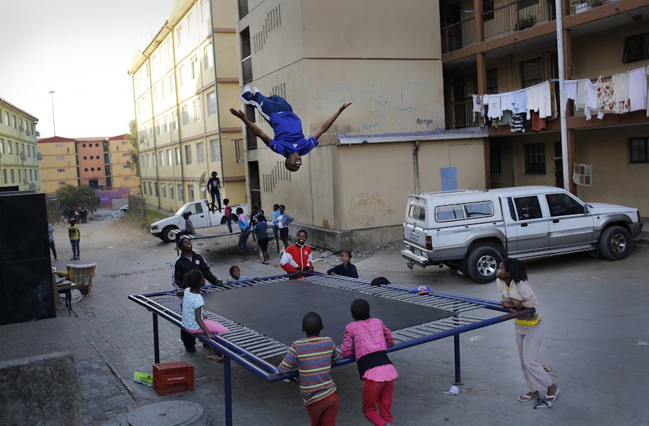A child jumps on a trampoline while others await their turn at a residential area made up of flats. 