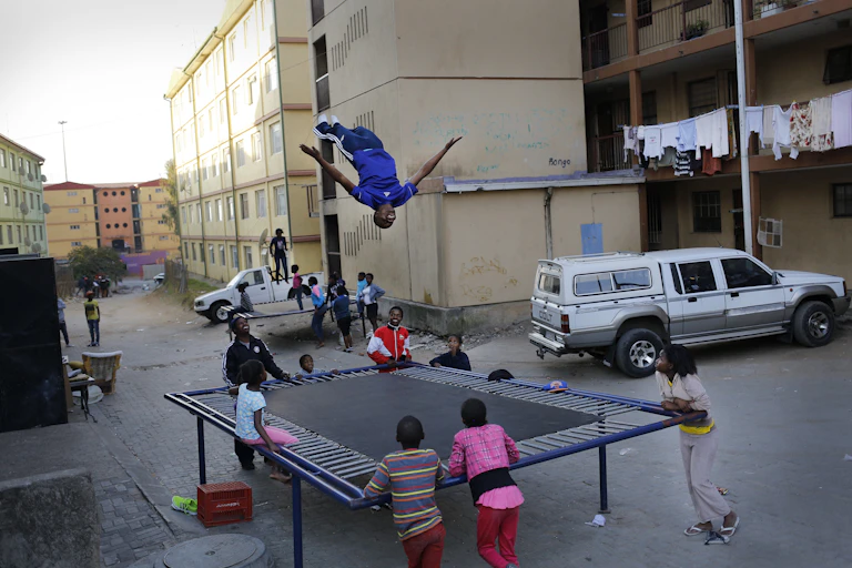 A child jumps on a trampoline while others await their turn at a residential area made up of flats.