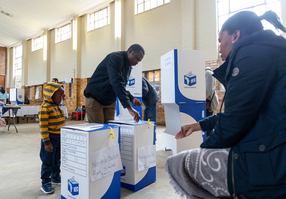 A man casts his ballot while a child looks on.