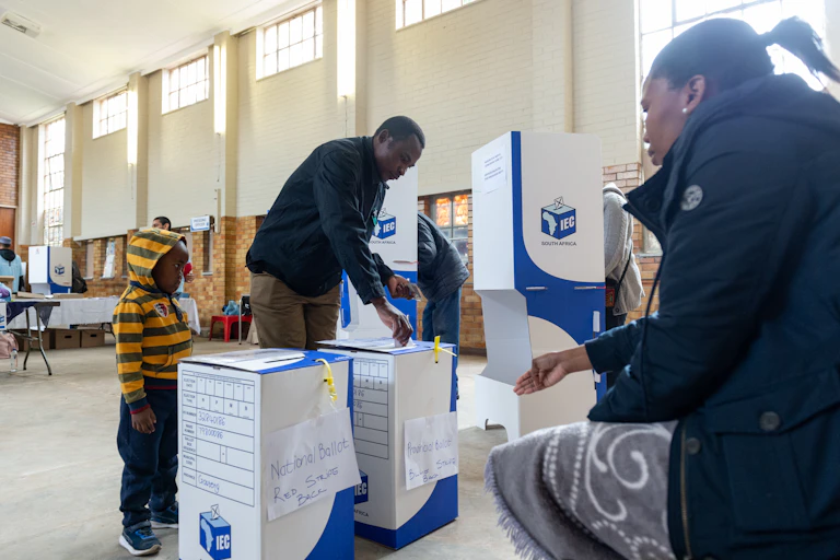 A man casts his ballot while a child looks on.