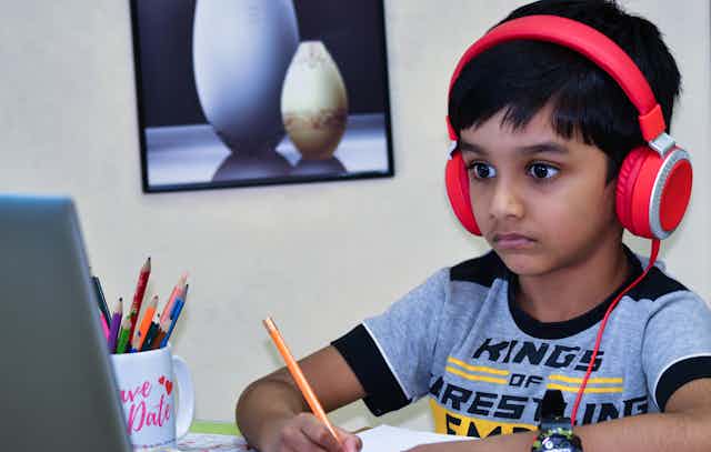 A boy in headphones looking at a laptop with a pencil.
