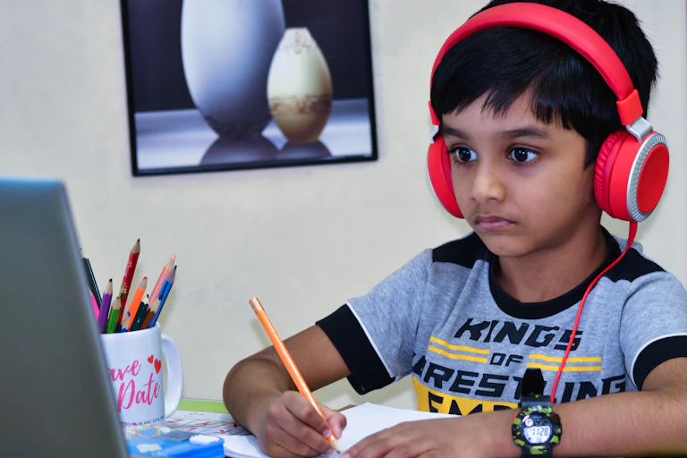 A boy in headphones looking at a laptop with a pencil.