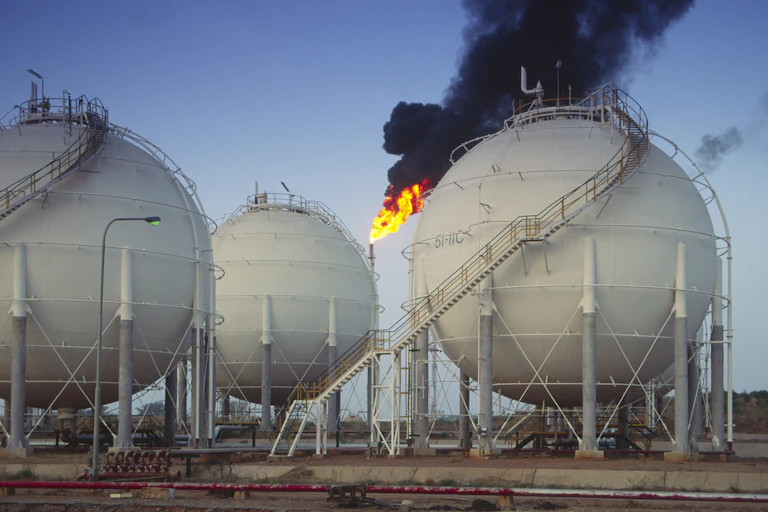 Large spherical structures supported by vertical pillars and with stairs around their exterior; flame and black smoke coming out of a vertical structure