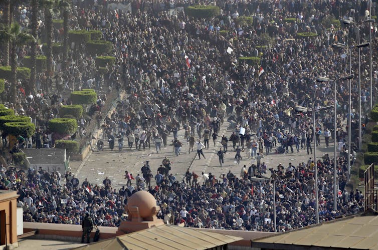 A crowd of people push through a wide street.