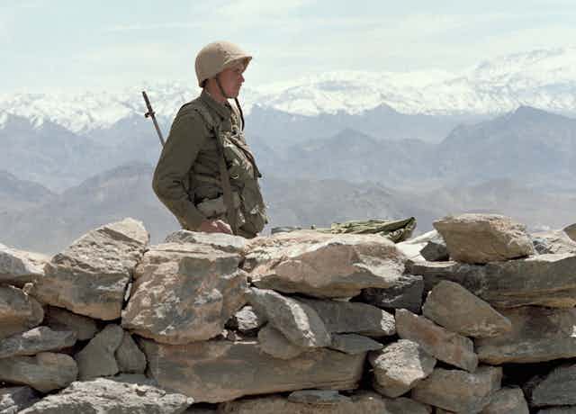 A Soviet soldier on guard in Afghanistan with snow-capped mountains in the background.