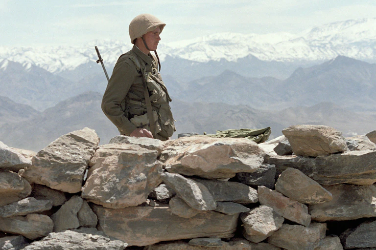 A Soviet soldier on guard in Afghanistan with snow-capped mountains in the background.