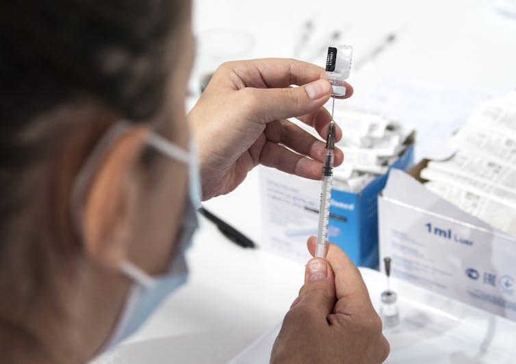 Masked nurse draws up a vial of COVID vaccine.