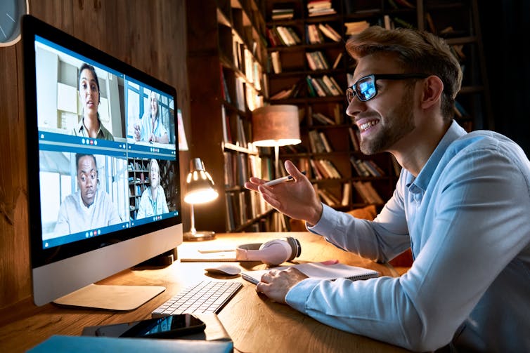 Young man smiles and gestures as group of young professionals meet online