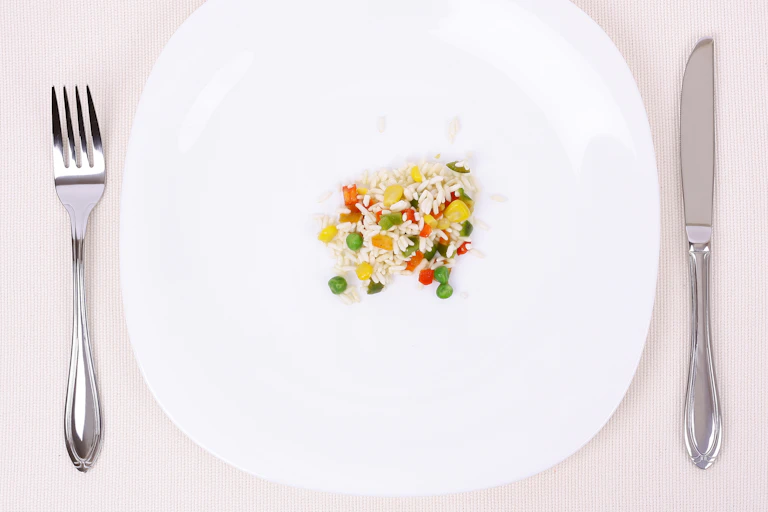 A white plat with a fork and knife on either side of it. There's a small portion of rice and vegetables in the centre.