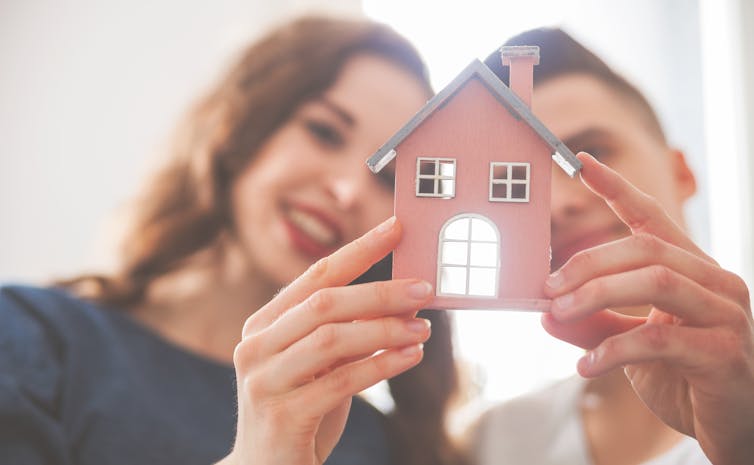 Two young people holding a tiny paper house.