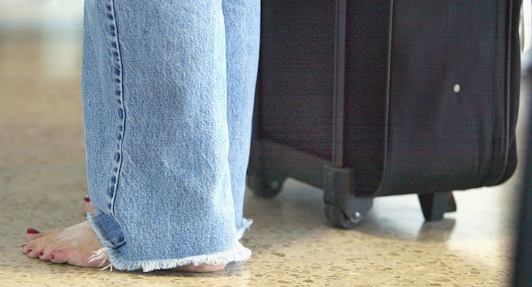 Barefoot woman stands next to her luggage.