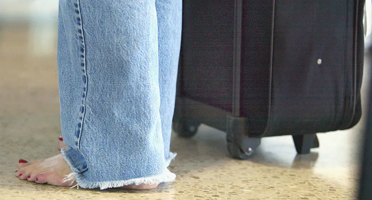 Barefoot woman stands next to her luggage.