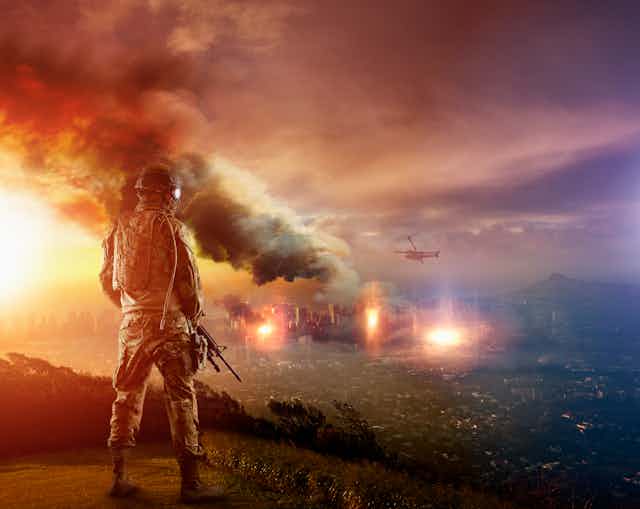 A soldier with a rifle overlooks plumes of smoke.
