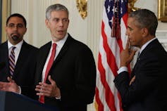 A man stands at a podium while two other men stand nearby.