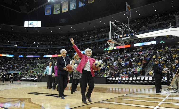 Bernice Sandler waves at people in the stands on a basketball court