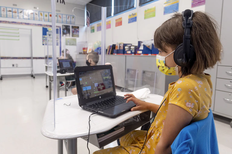 A young student works on a laptop at her desk in classroom