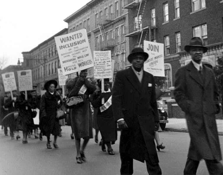 Black members of the Domestic Workers Union Members march down a road in protest.