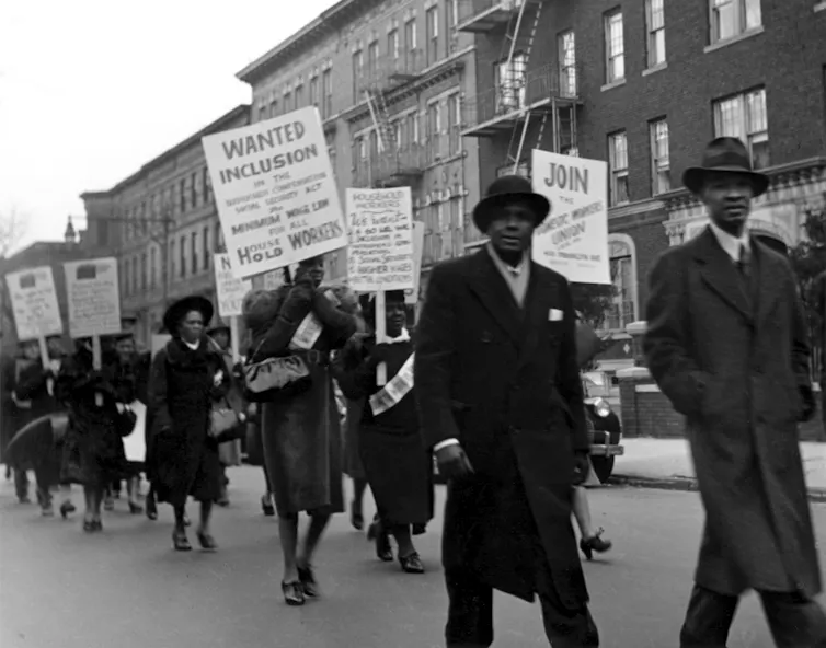 Black members of the Domestic Workers Union Members march down a road in protest.