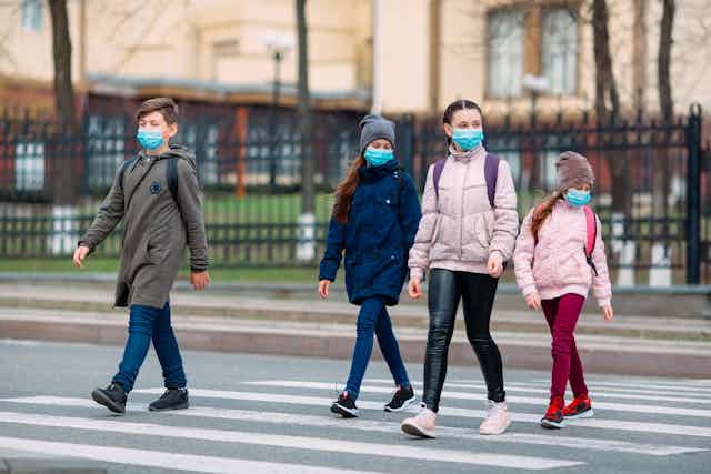 Kids wearing school bags and masks, crossing the road.