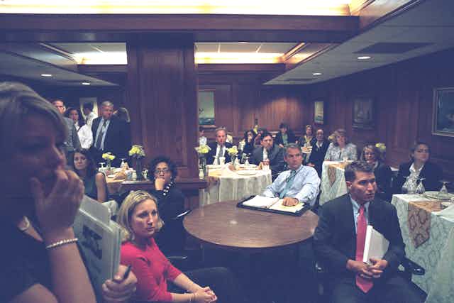 A lot of people in a large dining room, all looking concerned.