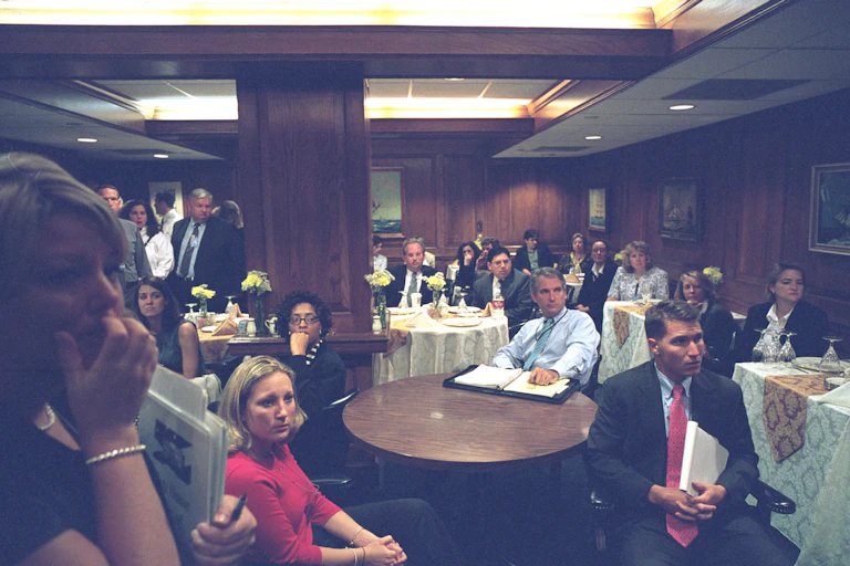 A lot of people in a large dining room, all looking concerned.