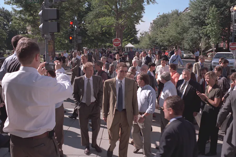 A crowd of people outside of the White House, on a street.