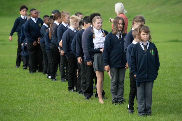 Children in school uniform queue on a playing field