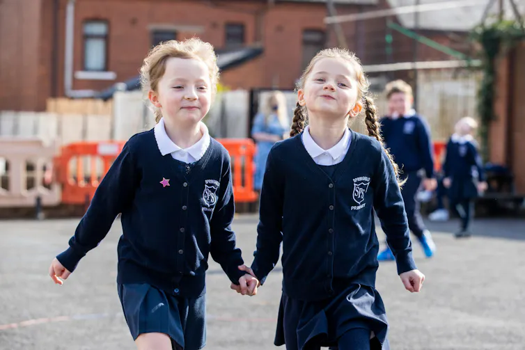 Two young girls hold on hands on the playground
