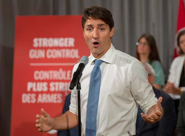 Trudeau speaks as he stands in front of a sign that says Stronger Gun Control.