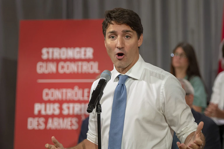 Trudeau speaks as he stands in front of a sign that says Stronger Gun Control.